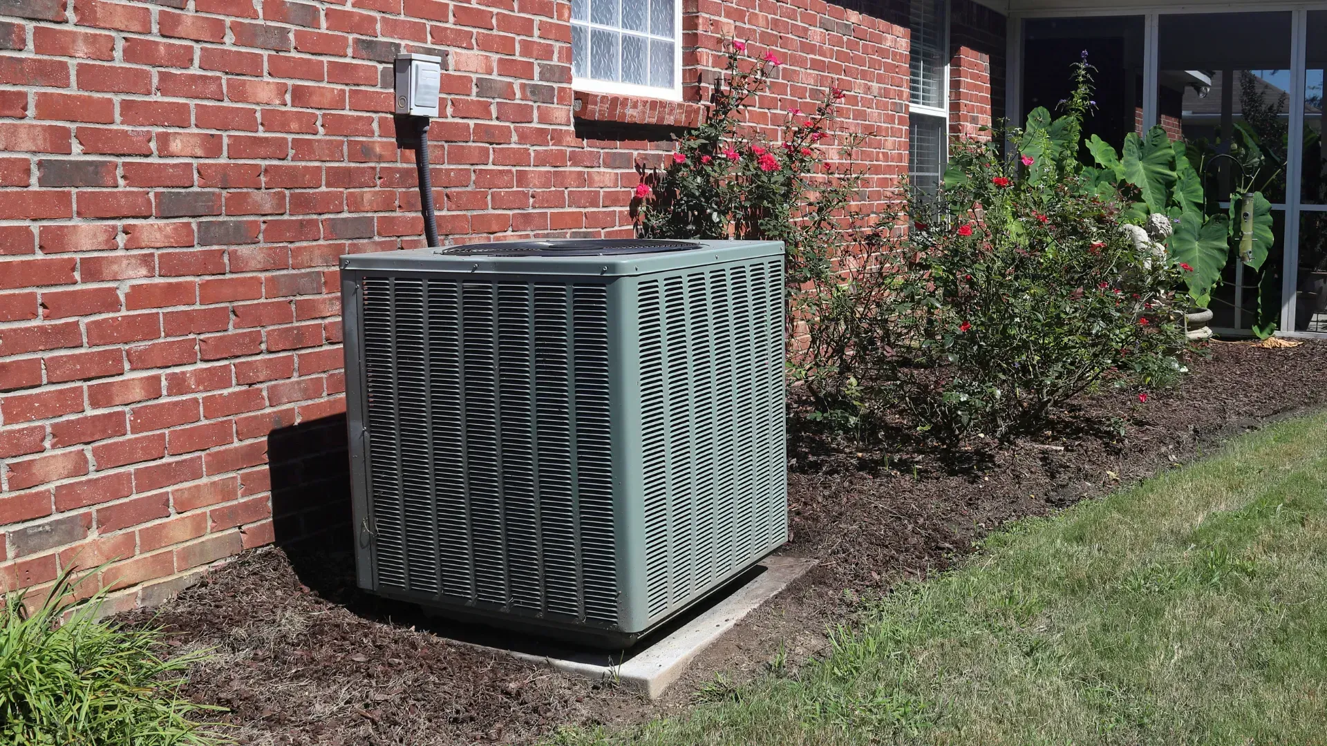 An air conditioner is sitting on the side of a brick house.
