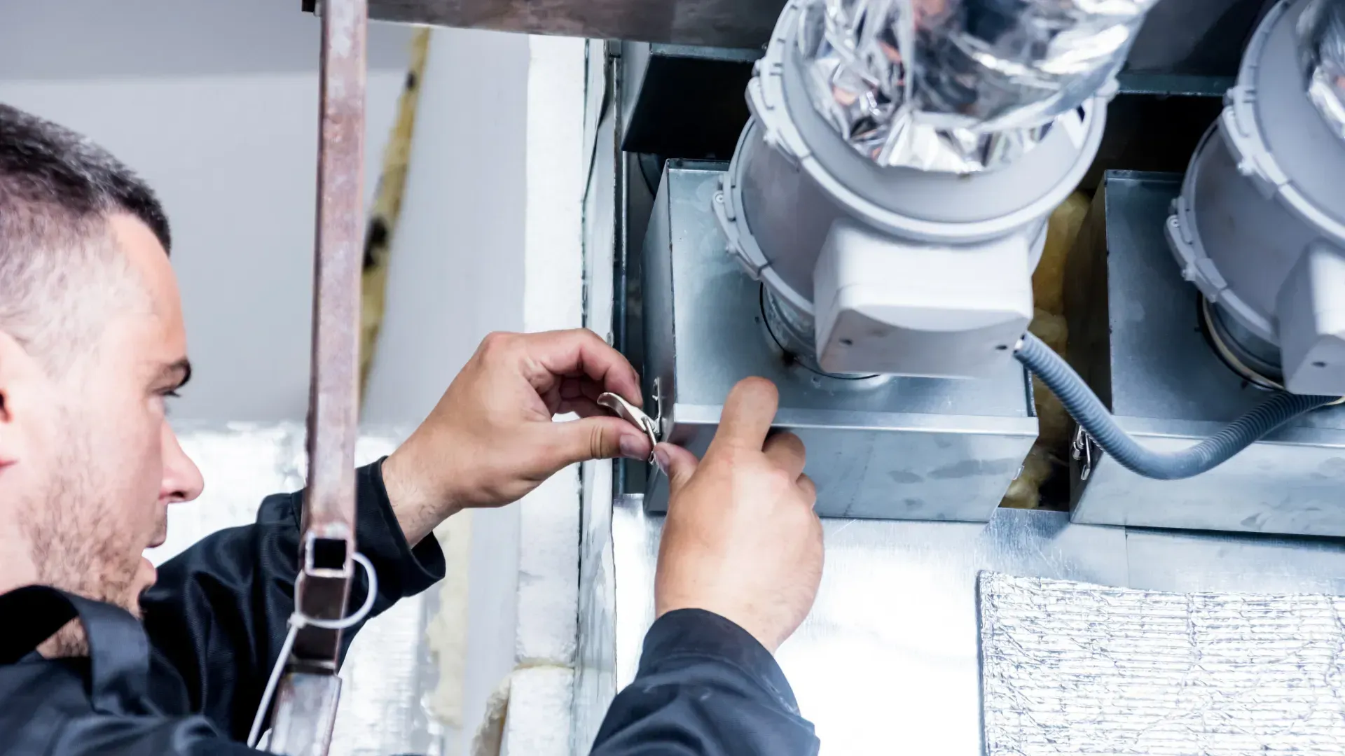 A man is working on a ventilation system in a building.