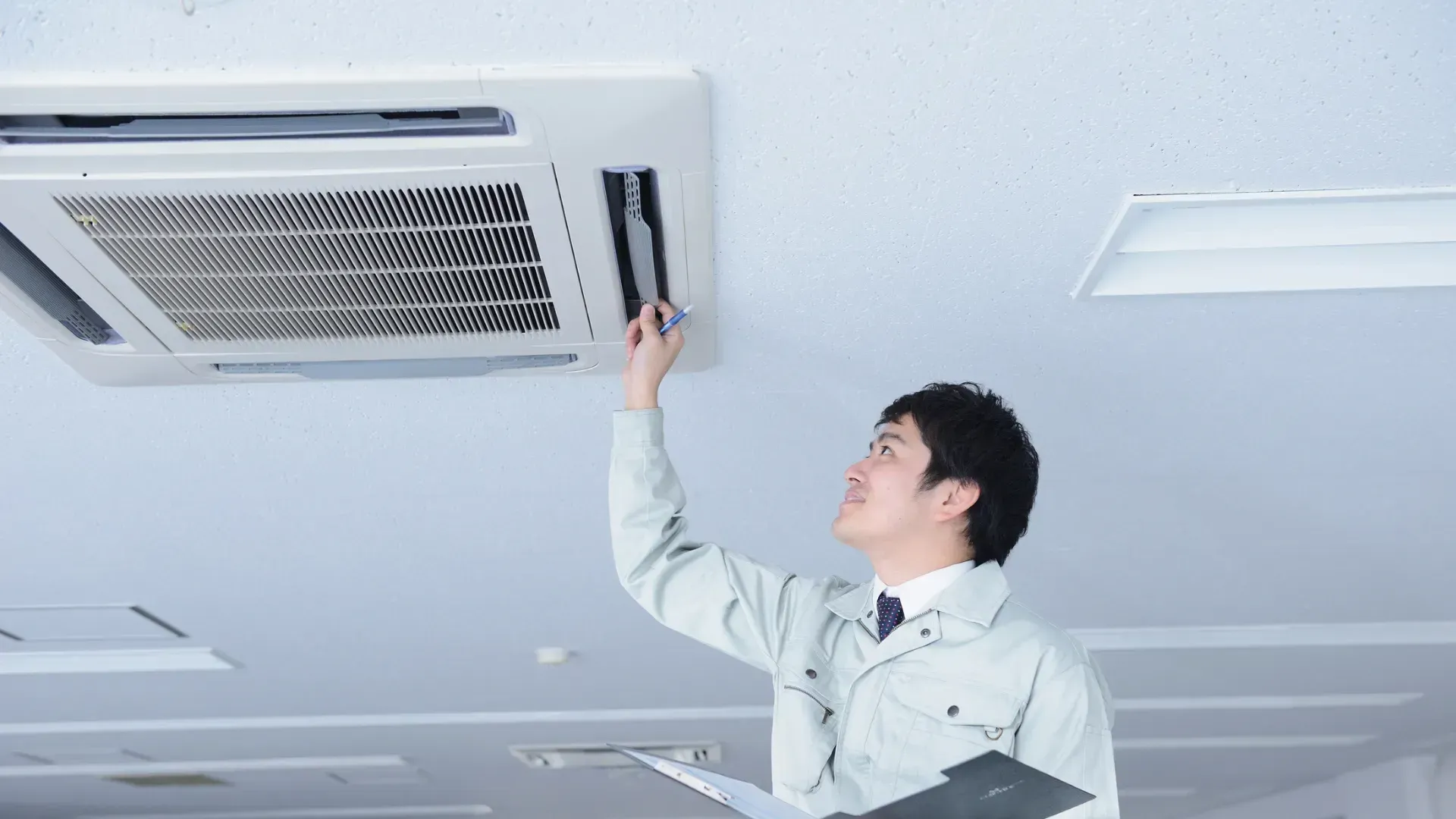 A man is looking at an air conditioner on the ceiling.