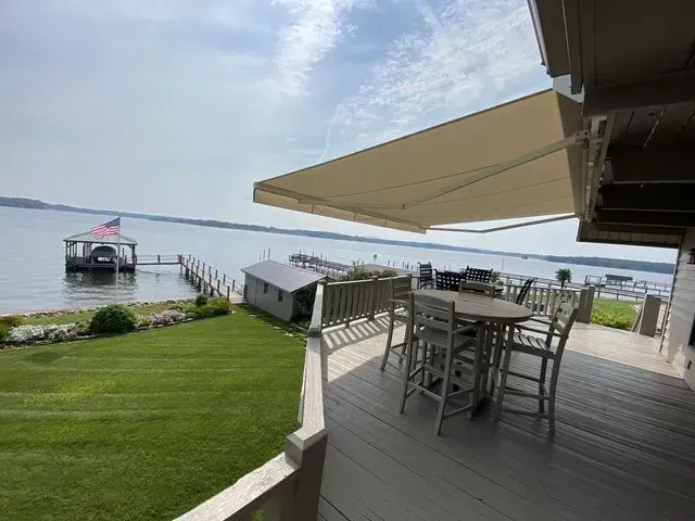 Waterfront deck with tables, umbrellas, lawn, and a docked boat on calm water
