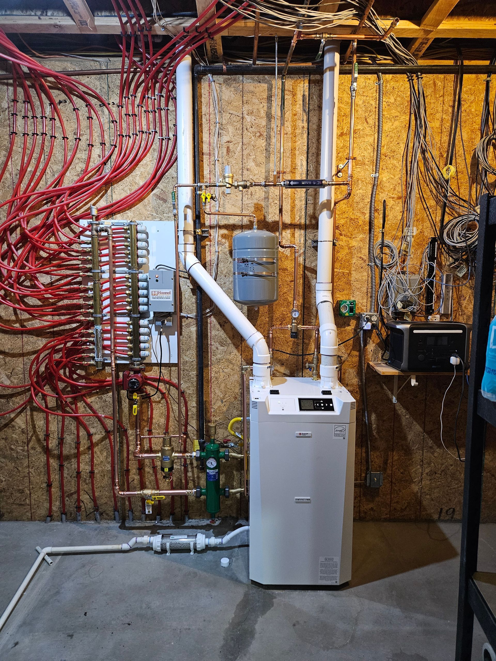 A white boiler is sitting in a basement next to a wall with a lot of wires hanging from it.