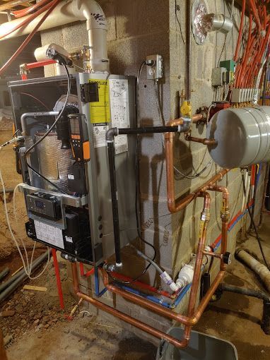 A boiler is being installed in a basement with copper pipes.