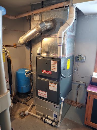 A furnace is sitting in a basement next to a water tank.