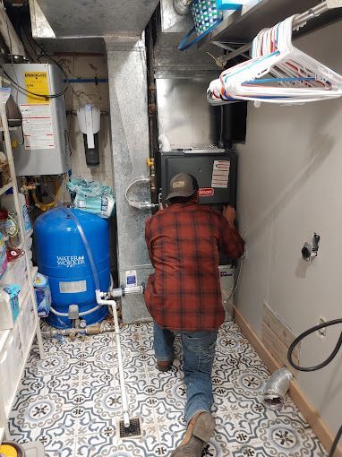 A man is working on a water heater in a laundry room.