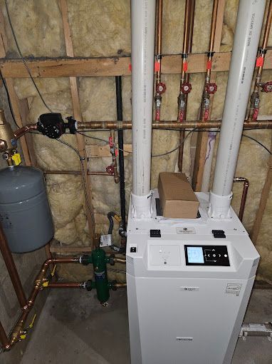 A white boiler is sitting in a room with copper pipes.