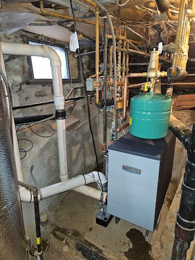 A boiler is sitting in a basement surrounded by pipes.