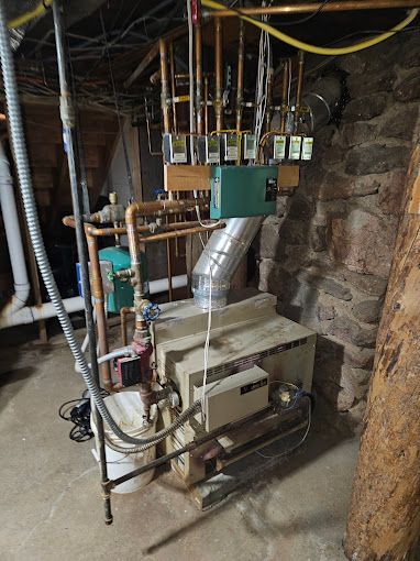 A boiler is sitting in a basement next to a stone wall.