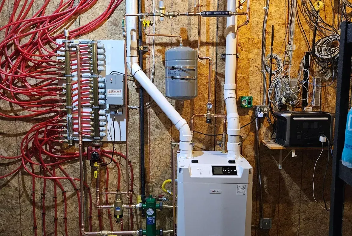A white boiler is sitting in a basement next to a wall with a lot of wires hanging from it.