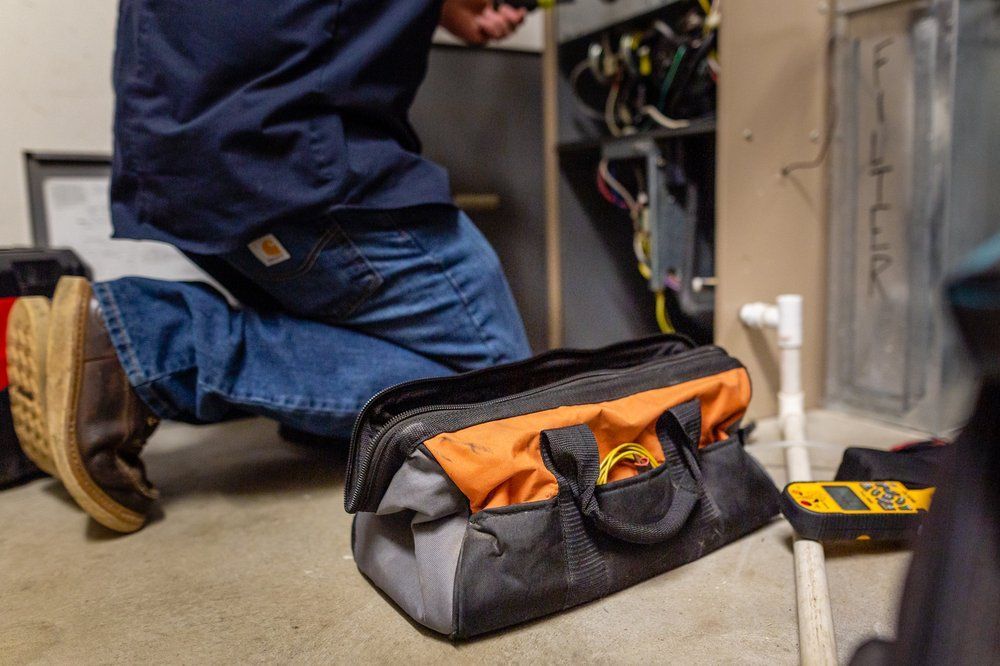 A man is kneeling down next to a tool bag in a room.