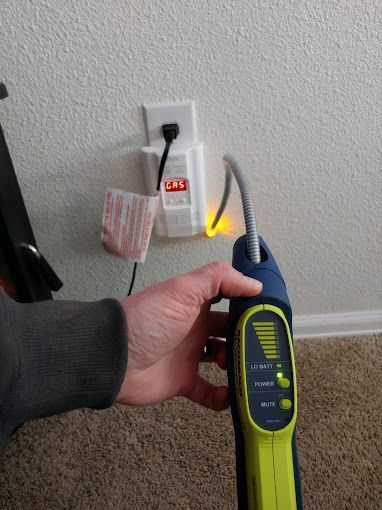 A person is holding a gas detector in front of a wall.