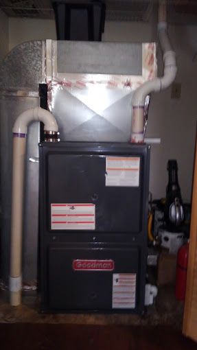 A furnace is sitting in a basement next to a pipe.