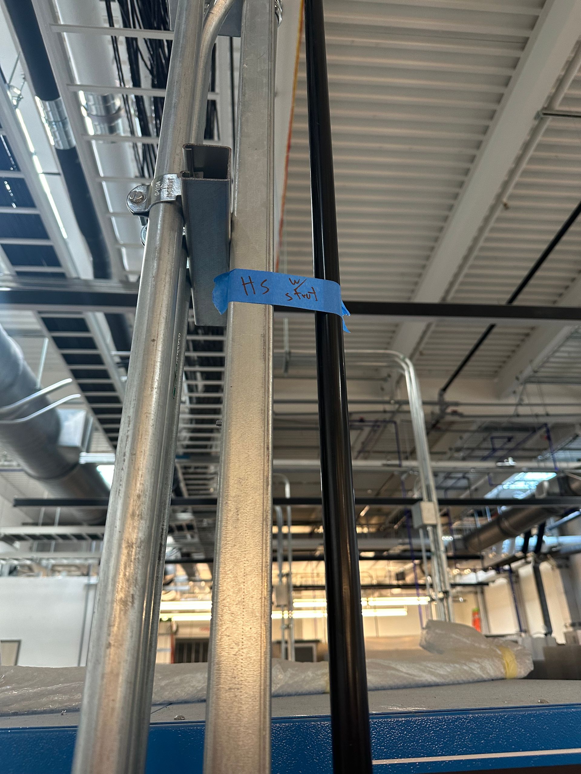 A blue tape is attached to a metal pipe in a building.