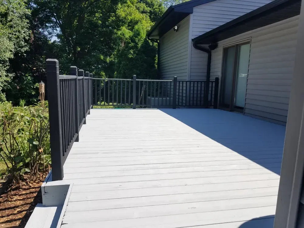 A white deck with a black railing in front of a house