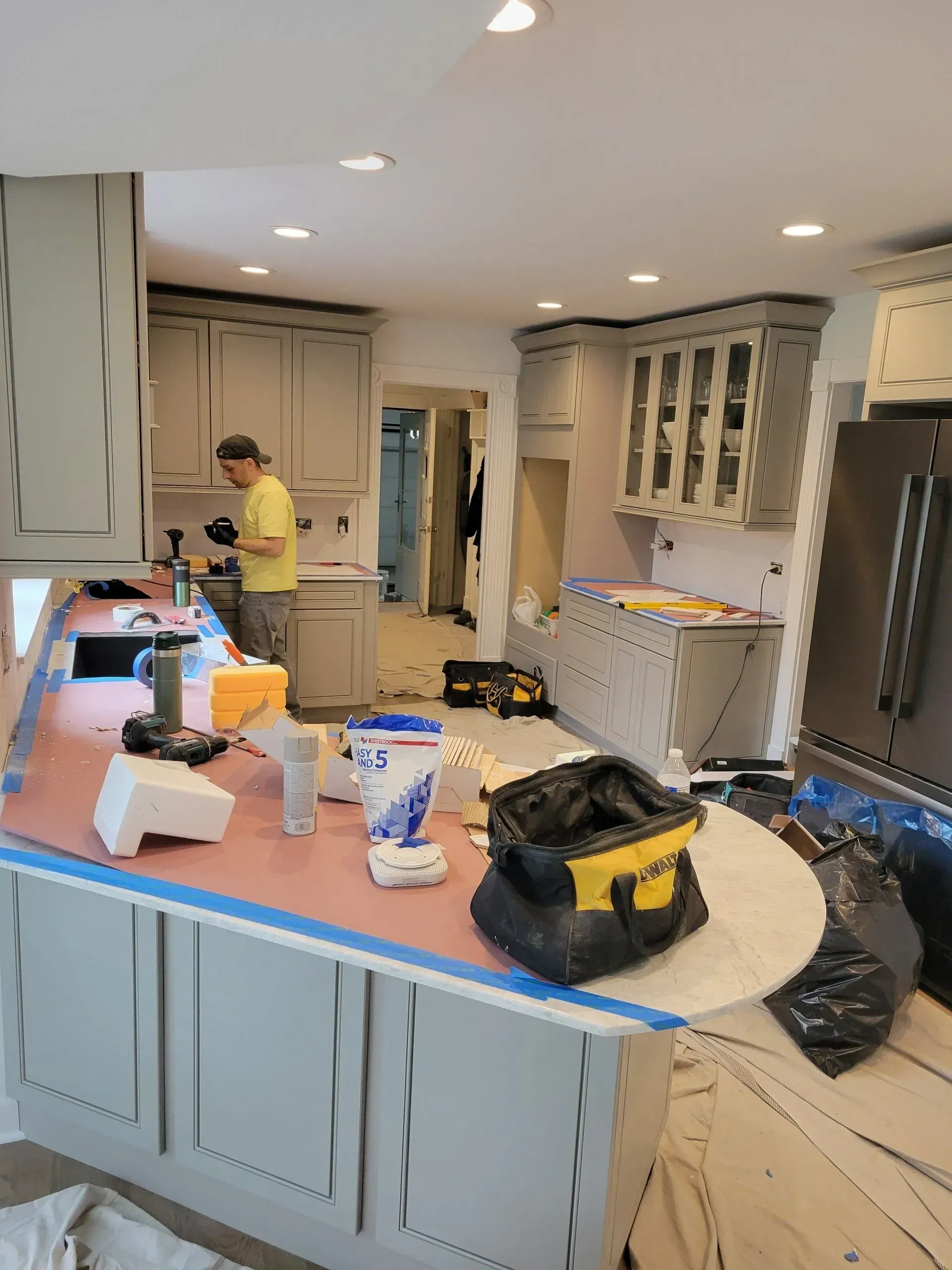 A man is standing in a kitchen painting cabinets.