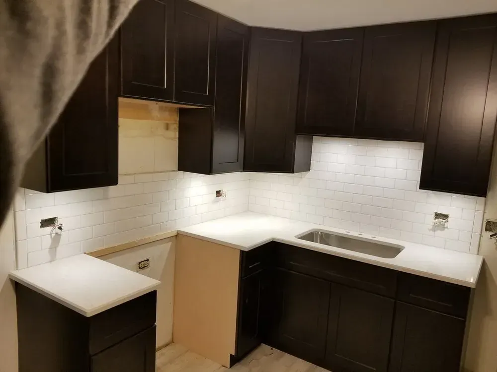 A kitchen with black cabinets and white counter tops and a sink.