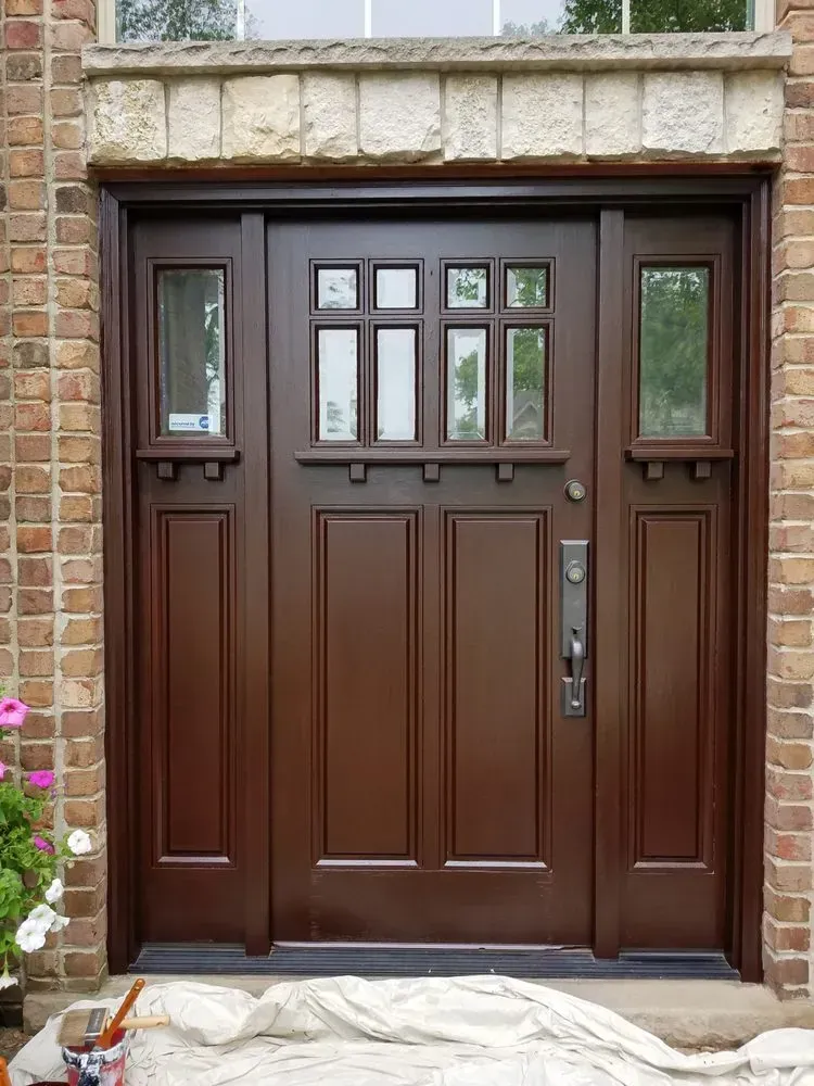 A brown door is being painted in front of a brick building.