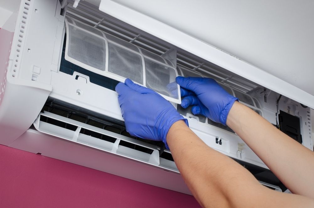 A Person Wearing Blue Gloves is Cleaning an Air Conditioner — Airac Sales & Service in Berserker, QLD