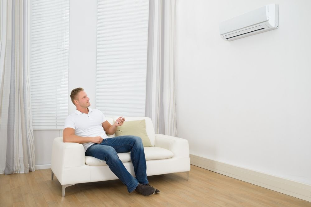 A Man is Sitting on a Couch in Front of an Air Conditioner in a Living Room — Airac Sales & Service in Yeppoon, QLD