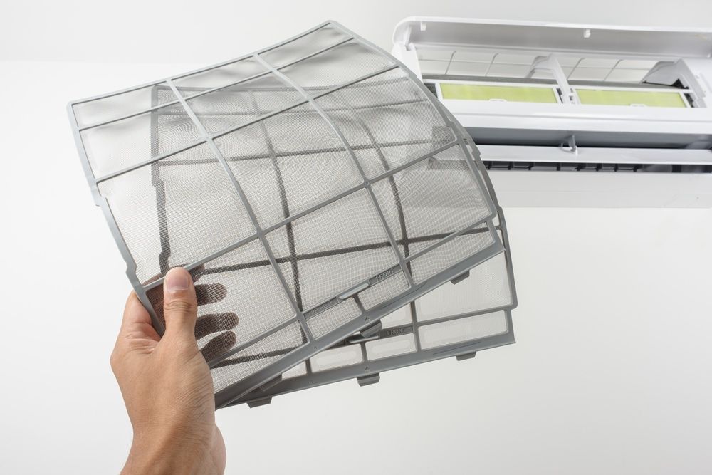 A Person is Holding a Dirty Air Filter in Front of an Air Conditioner — Airac Sales & Service in Gracemere, QLD