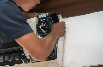 A Man is Fixing an Air Conditioner on a Wall — Airac Sales & Service in Berserker, QLD