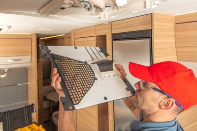 A Man in a Red Hat is Holding a Piece of Metal in a Camper — Airac Sales & Service in Berserker, QLD