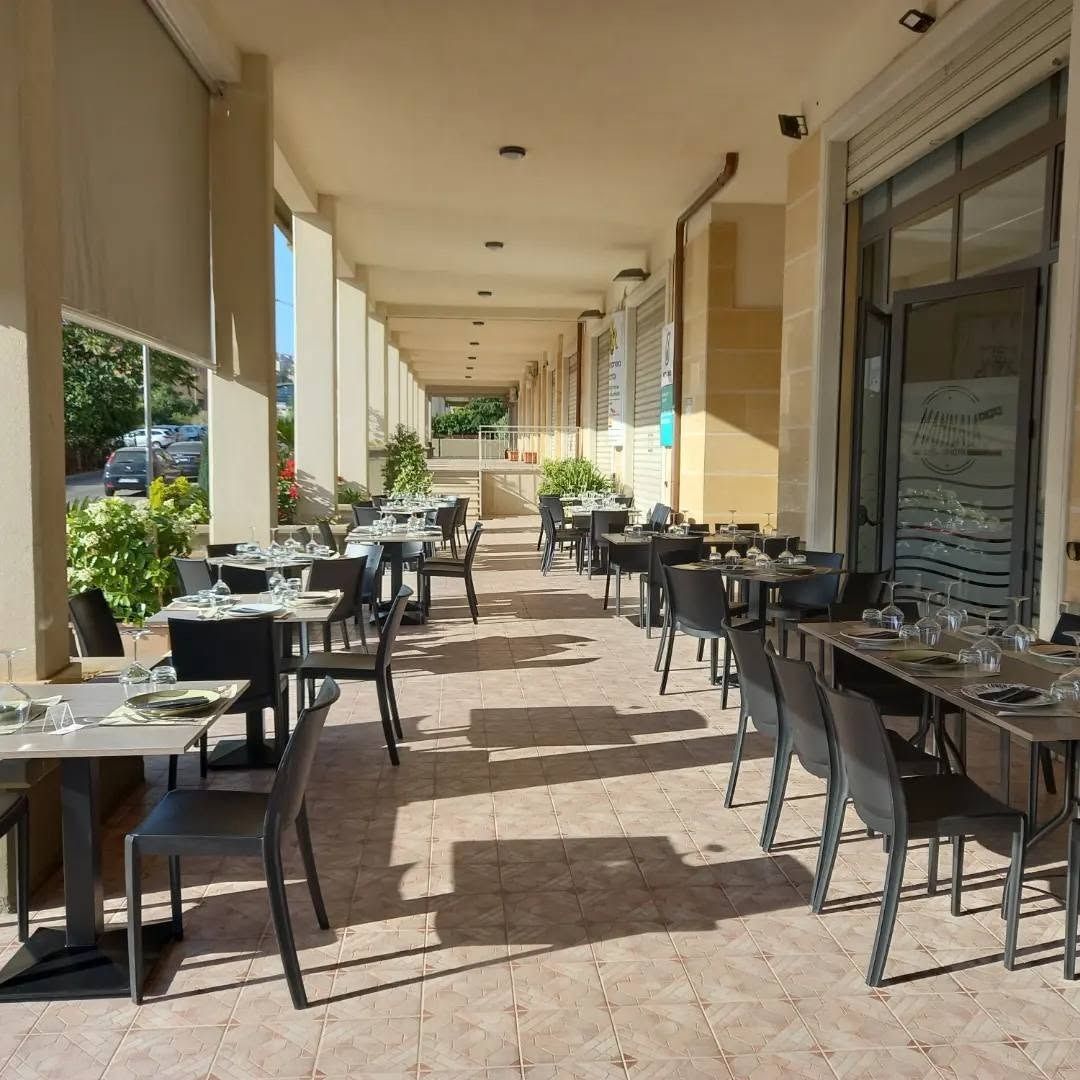 Terrazza esterna del ristorante con tavoli e sedie vuoti sotto una tettoia.
