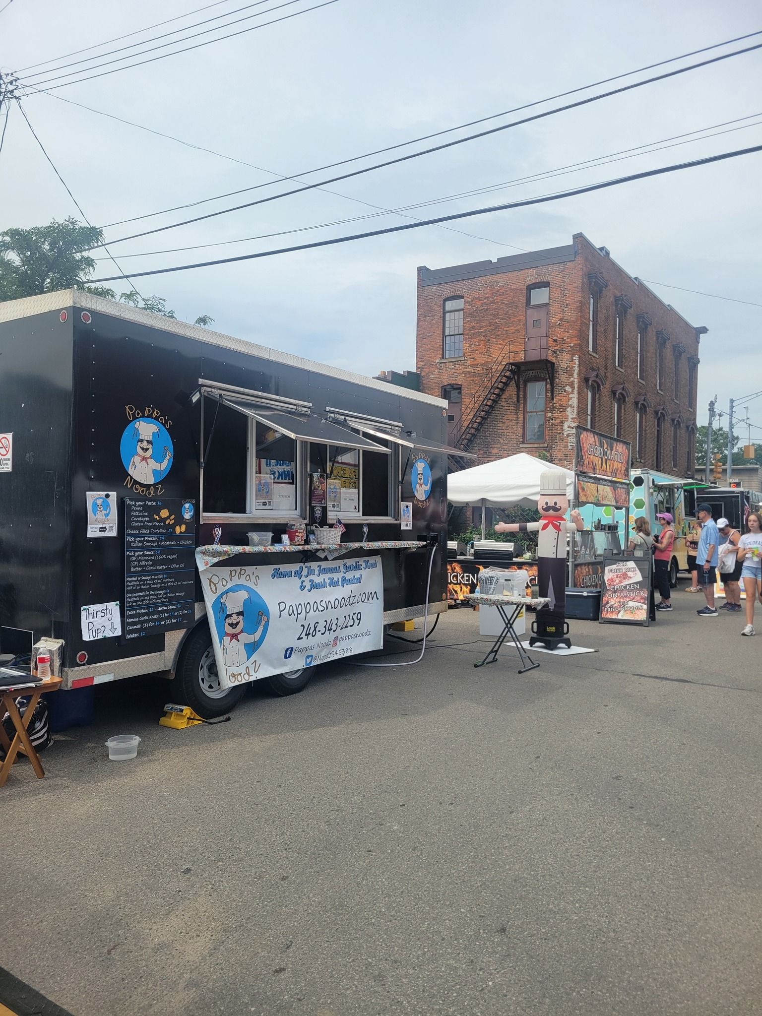 Outdoor street market with food trucks, tents, and people gathered on a cloudy day.