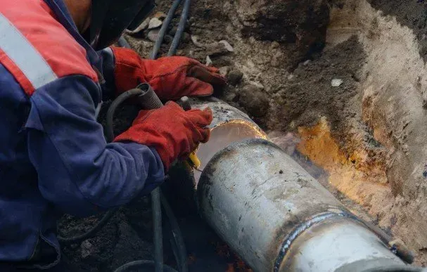 A man is welding a pipe in the dirt.