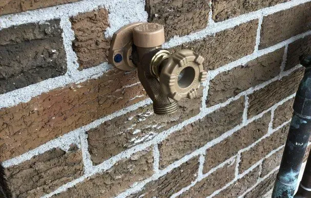 A close up of a faucet on a brick wall.