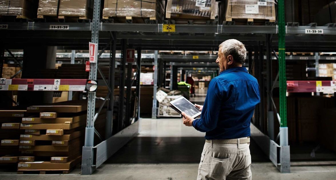 A man is standing in a warehouse holding a tablet.