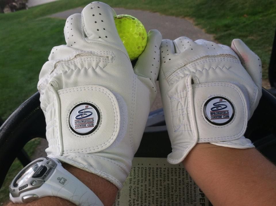 Golfers on a green with a church and houses in the background on a sunny day.
