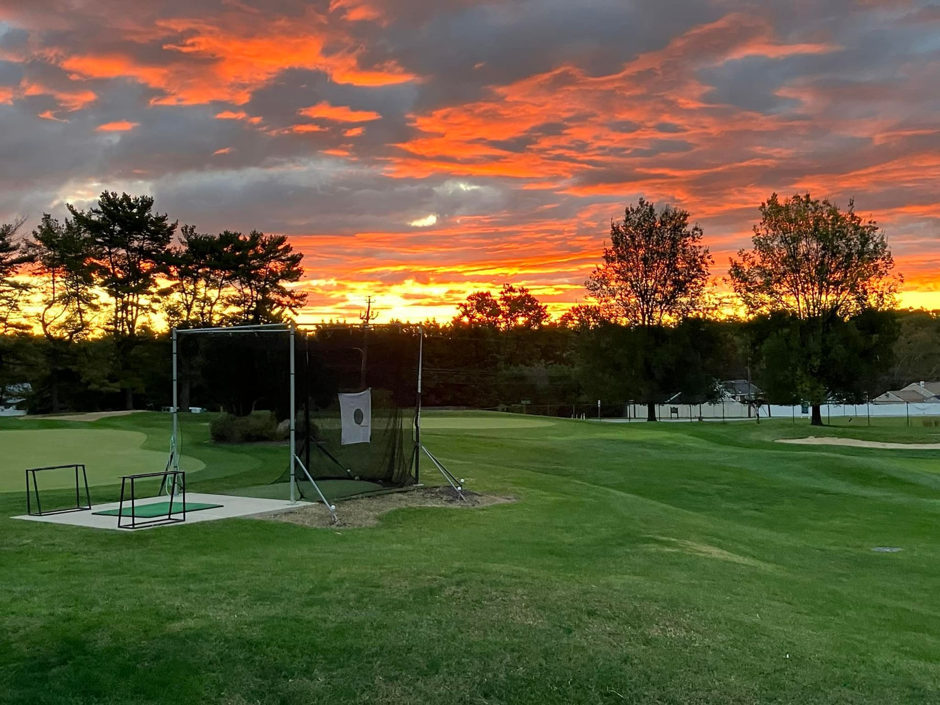 A person swings a golf club on a driving range, other people watch. Bright sunny day.