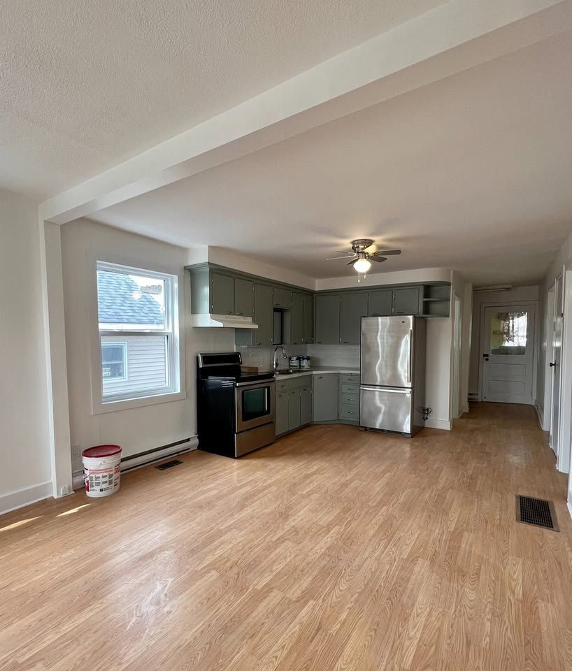 A kitchen with a stove , refrigerator , and sink in an empty house.
