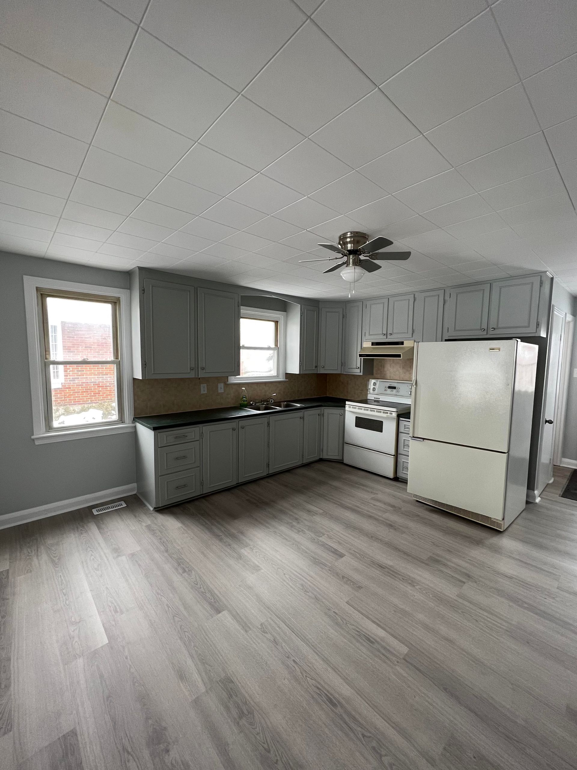 An empty kitchen with a stove , refrigerator , and ceiling fan.