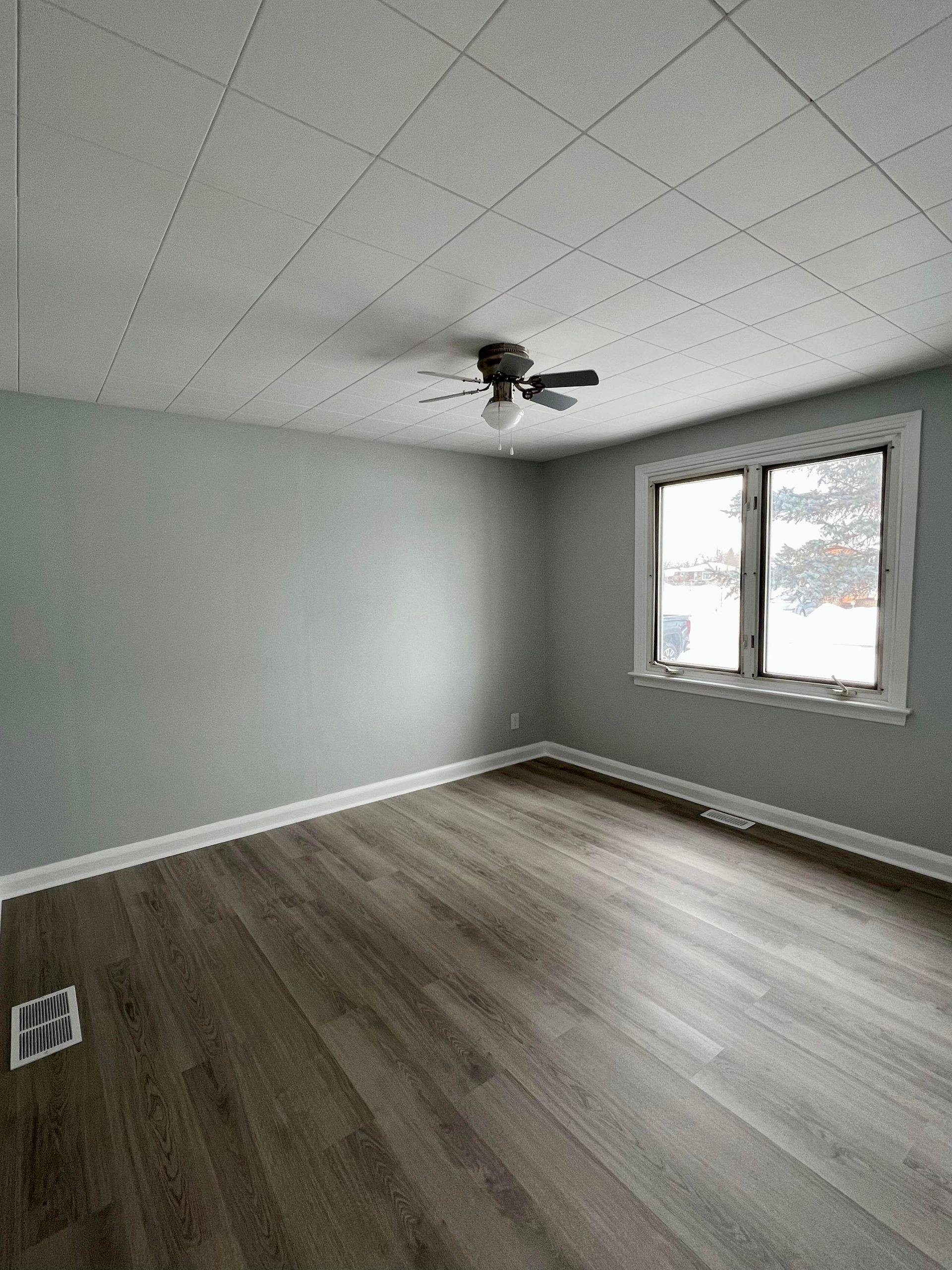 An empty room with a ceiling fan and two windows.