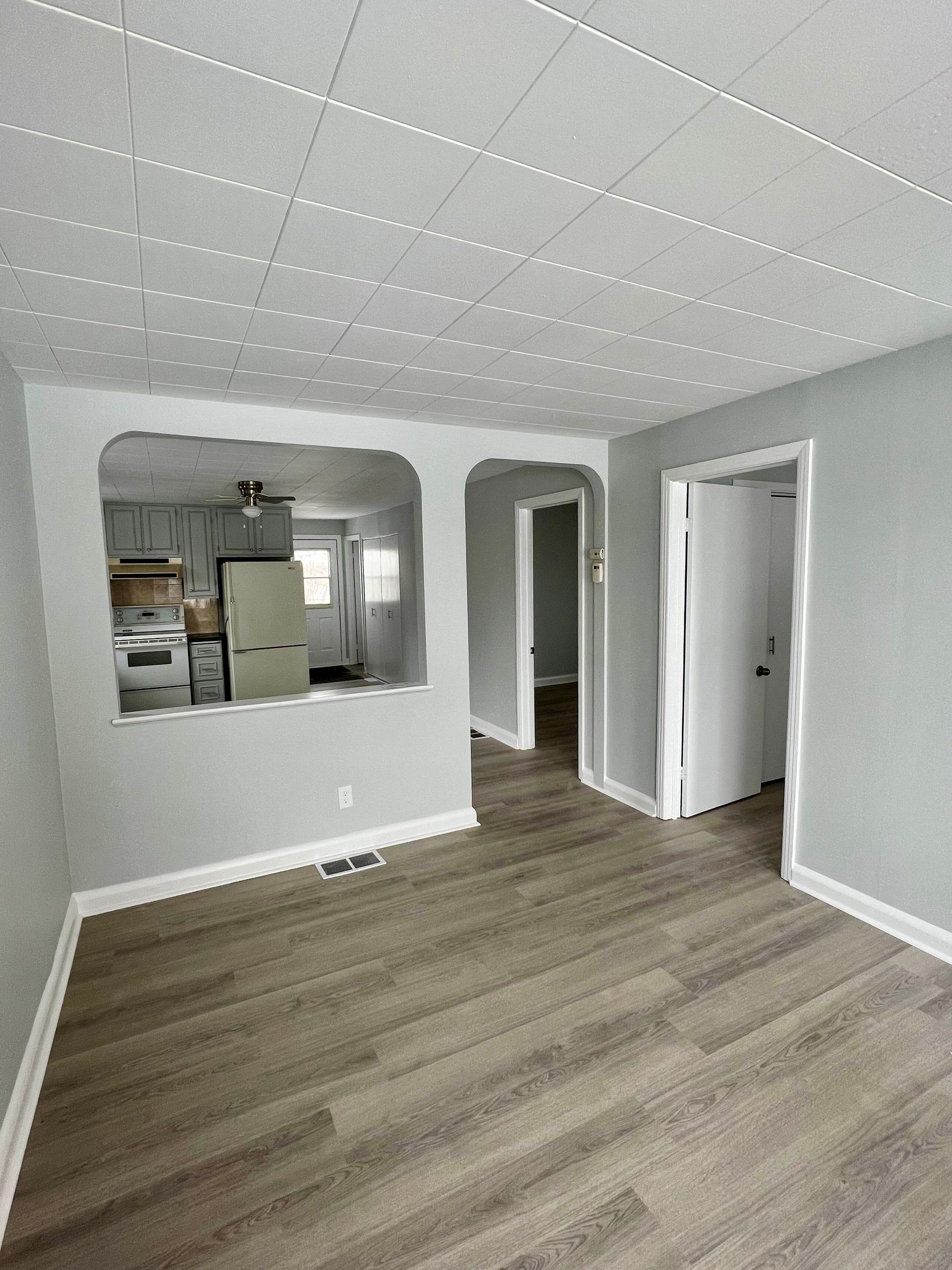 A living room with hardwood floors and a kitchen in the background.