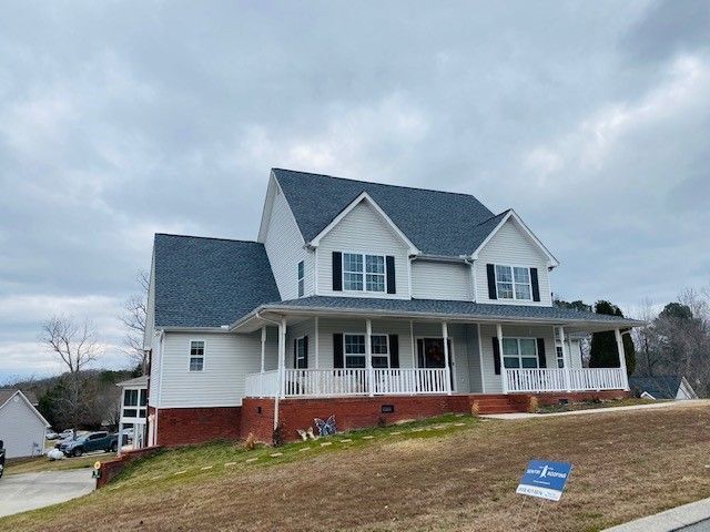 Two-story white house with black shutters, a covered porch, and a dark gray roof on a slightly elevated lot under a cloudy sky.