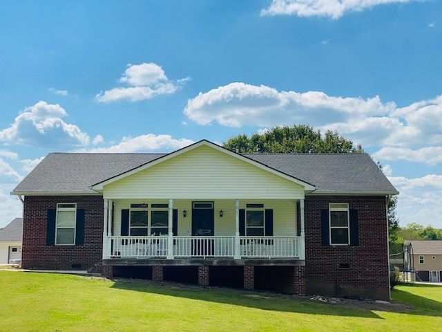 Brick and white house with porch under a blue sky with fluffy clouds.