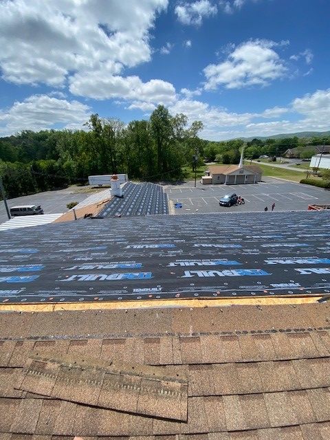 A roof in progress, with new underlayment being installed over old shingles, church in the background on a sunny day.