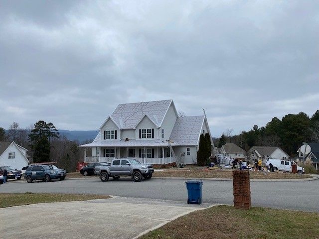 A two-story white house with a porch. Cars and a blue trash can are in the foreground, cloudy sky above.