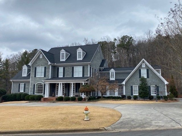 Large gray house with a dark roof, white trim, and a curved driveway on a cloudy day.