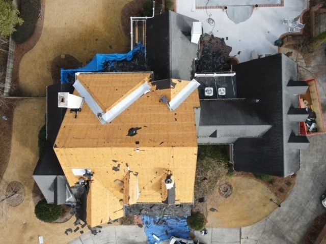 Overhead view of a house with roof damage and debris; portions covered with blue tarp.