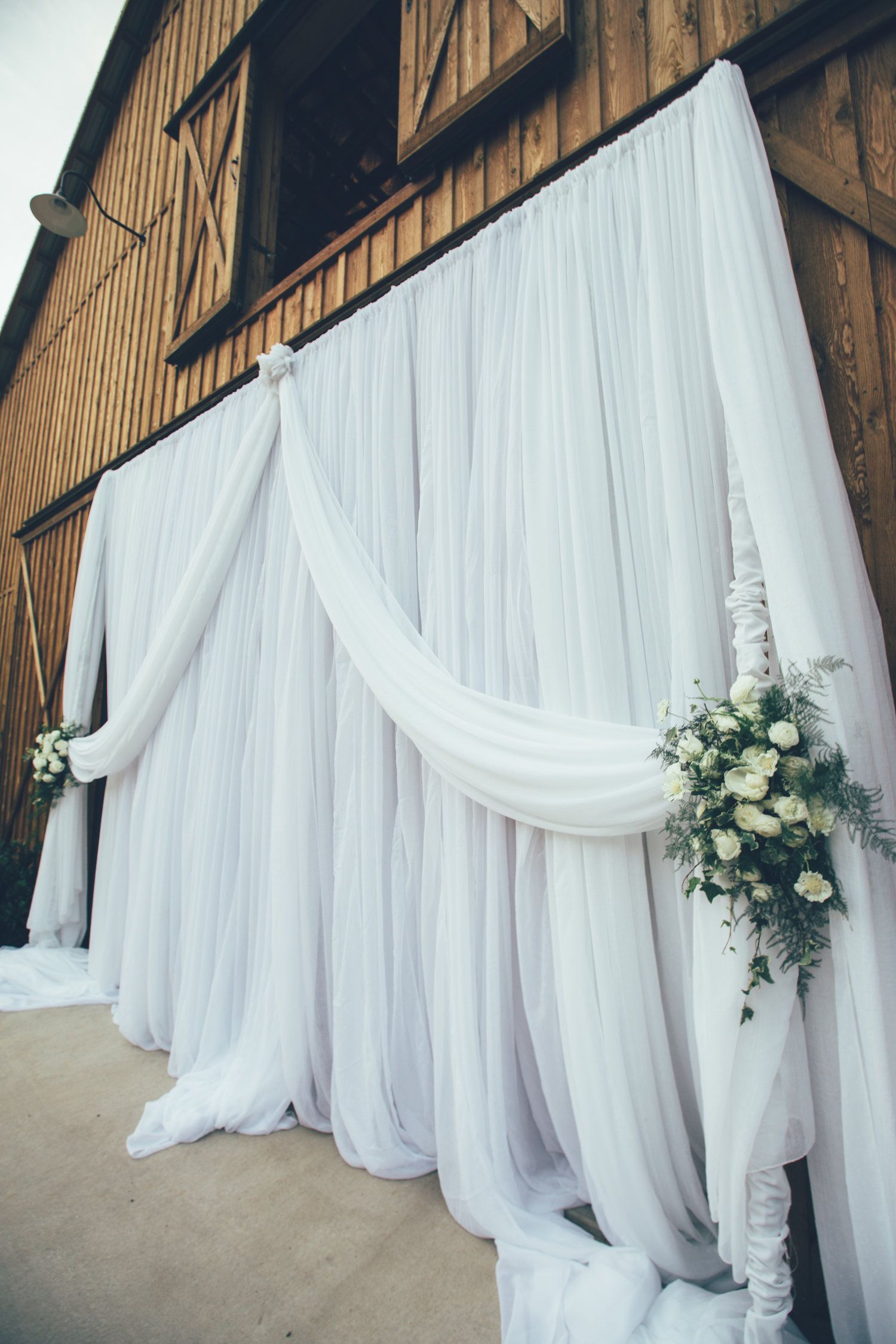 Hannah and Dustin's Wedding white curtain with flowers on it is hanging on a wooden wall by Wedding Planner Nashville