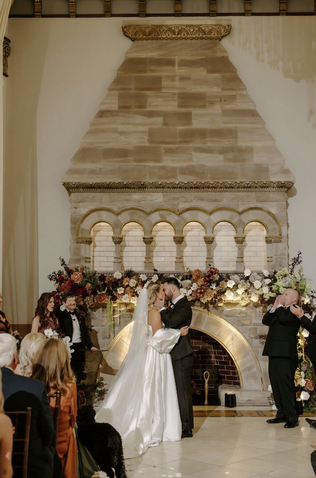 Couple kisses at wedding ceremony in front of a stone fireplace decorated with floral arrangements by Luxury Wedding Planners in Nashville, TN