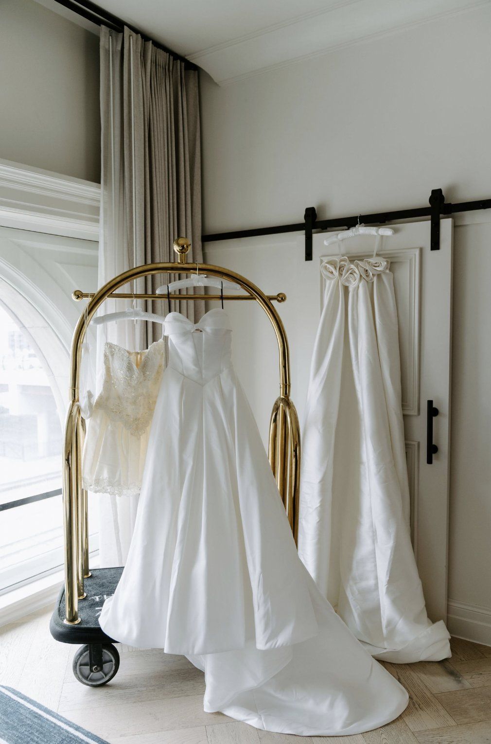 Wedding dresses hanging in a room: A-line gown on a golden rack, a smaller dress, and a long veil by Luxury Wedding Planners in Nashville, TN