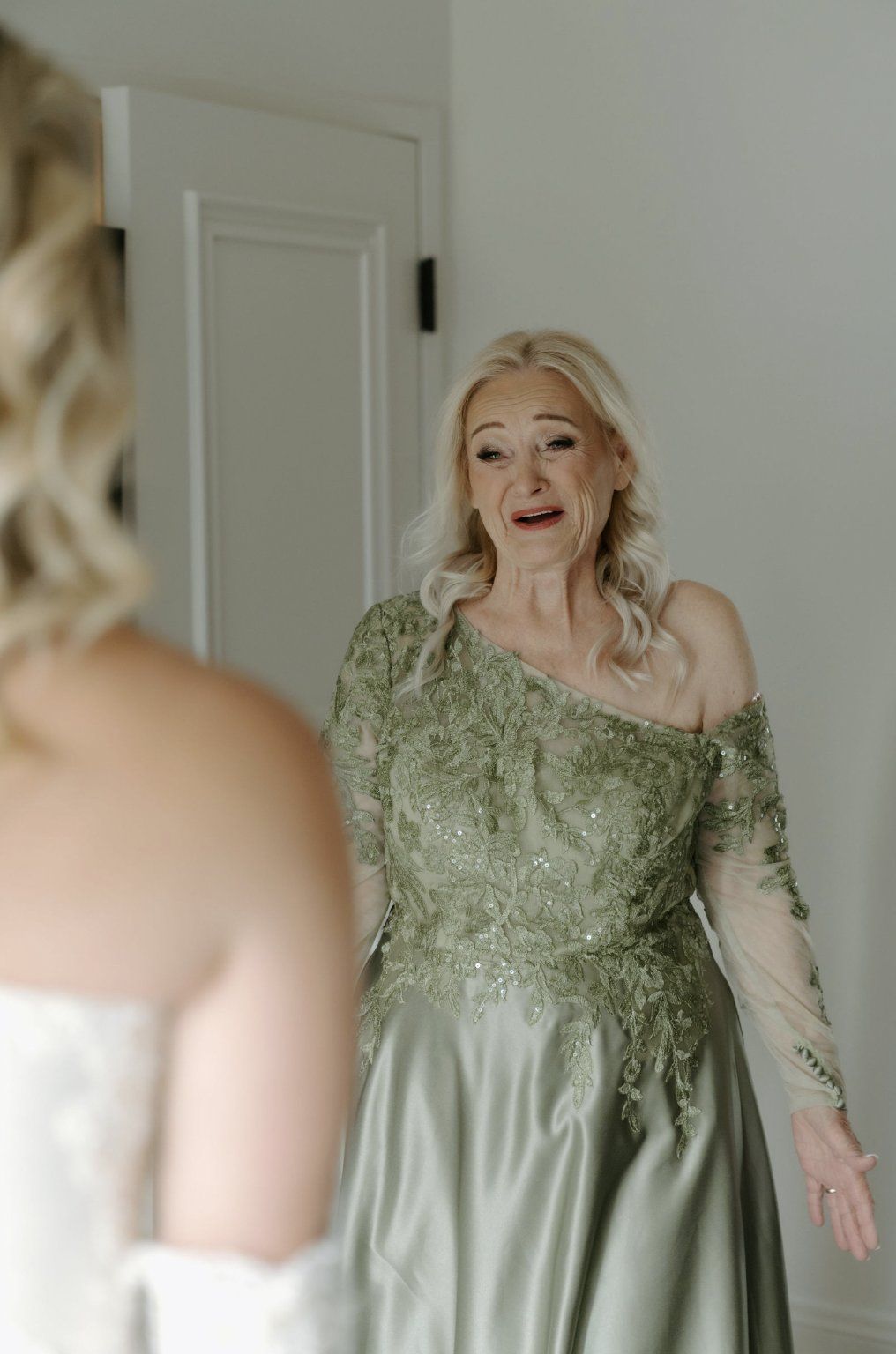Woman in green dress looks at bride in wedding dress, surprised expression, indoor setting by Luxury Wedding Planners in Nashville, TN