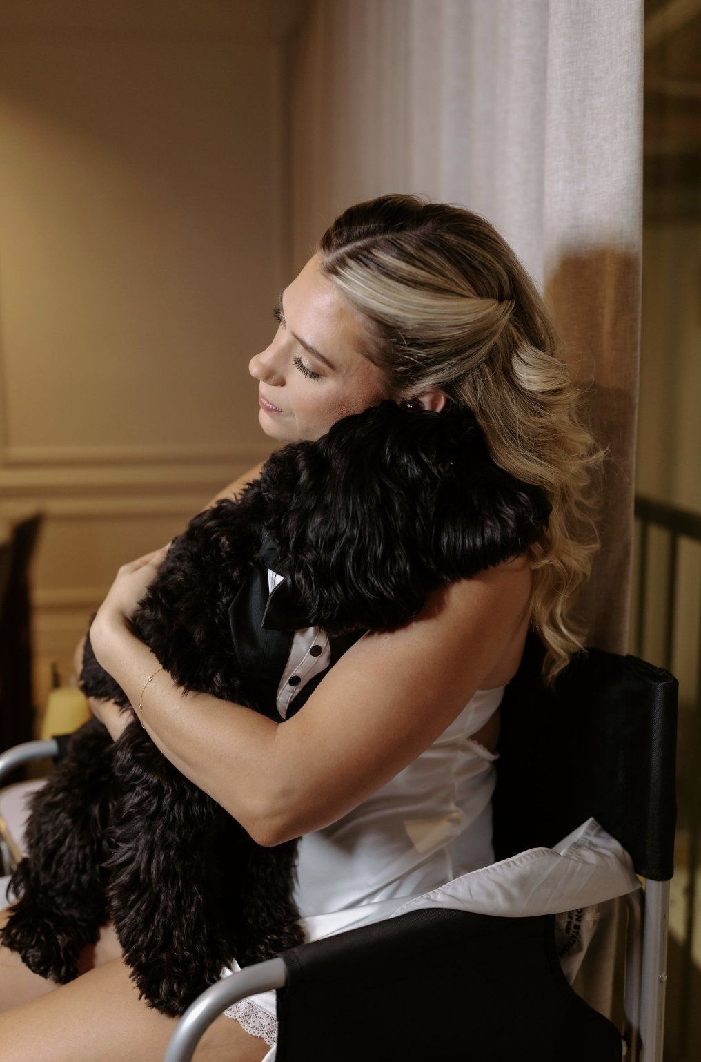 Woman hugging a small black dog indoors, likely a dressing room by Luxury Wedding Planners in Nashville, TN