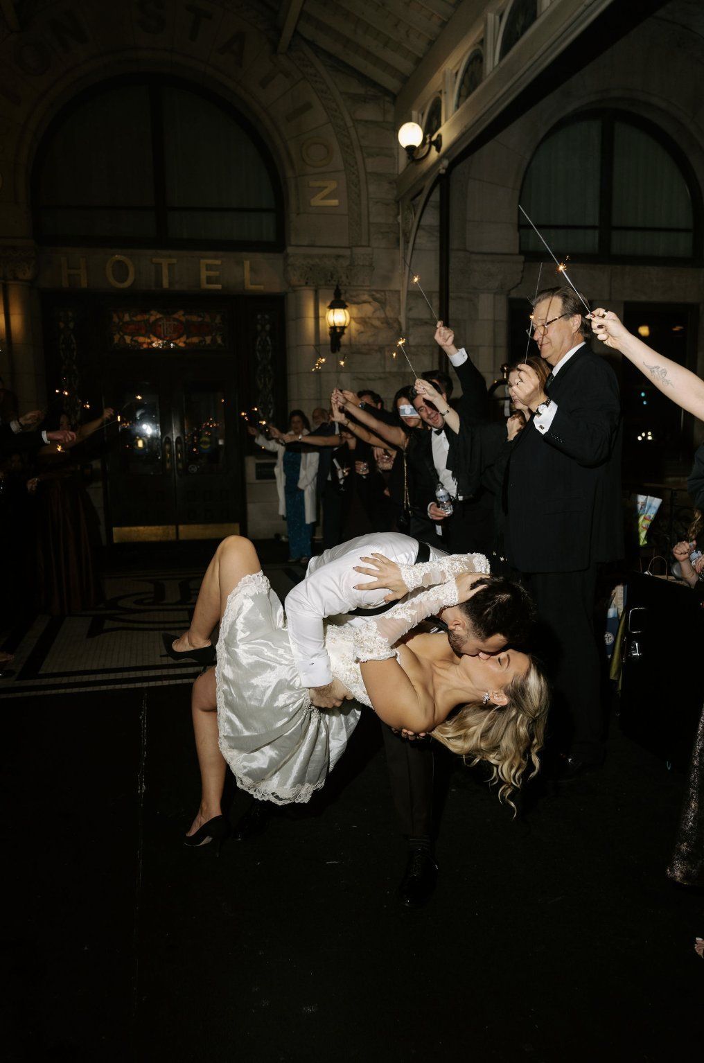 Bride and groom kiss, dipped backward, held by the groom as wedding guests hold sparklers outside a hotel by Luxury Wedding Planners in Nashville, TN