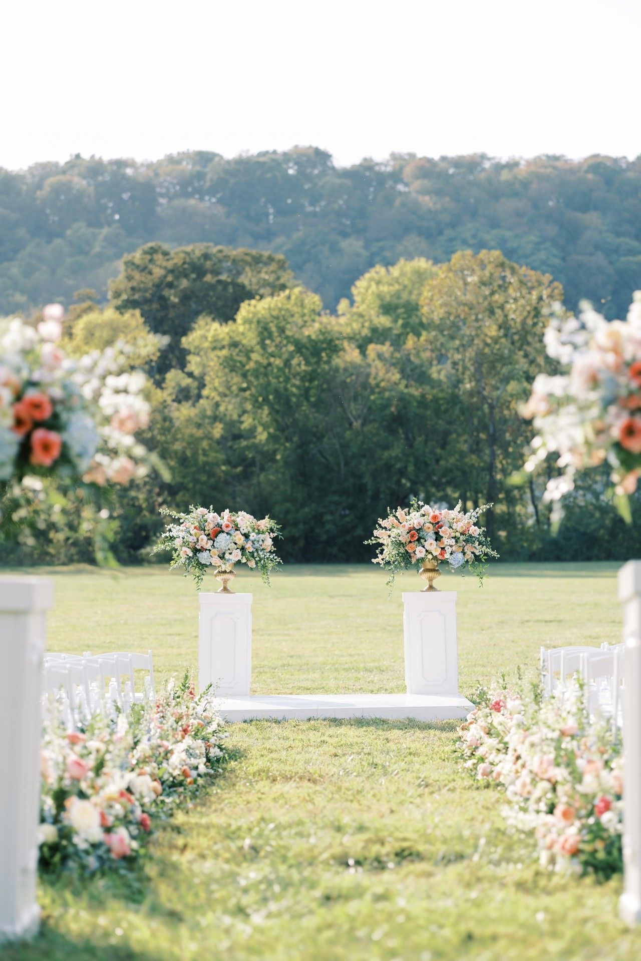 A wedding ceremony is taking place in a field with flowers on pedestals by Luxury Wedding Planners in Nashville, TN