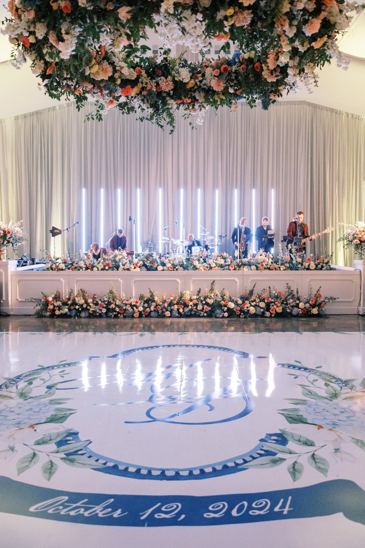 A dance floor with a monogram on it and flowers hanging from the ceiling by Luxury Wedding Planners in Nashville, TN